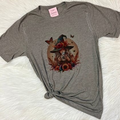 Gray t-shirt with a colorful graphic of a woman in a hat and flowers on a white surface