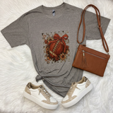 A styled flat-lay featuring an ash gray t-shirt with a football graphic, paired with a brown faux leather crossbody bag and white/beige sneakers, all arranged on a white faux fur background.