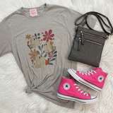 A styled flat-lay outfit featuring a light gray t-shirt with a ghost graphic, a dark gray crossbody bag, and a pair of bright pink high-top sneakers, arranged on a white faux fur background.