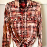A long-sleeve plaid button-up shirt in red, brown, and beige tones, styled tied at the hem and hanging against a white background.