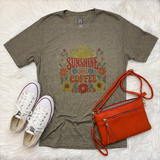 A styled flat-lay featuring a heathered sage green graphic t-shirt with a retro 'SUNSHINE AND COFFEE' floral print, accompanied by white Converse sneakers and an orange crossbody bag on a white faux fur background.